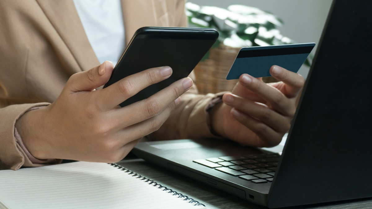 Person sitting in front of laptop holding a phone and credit card.