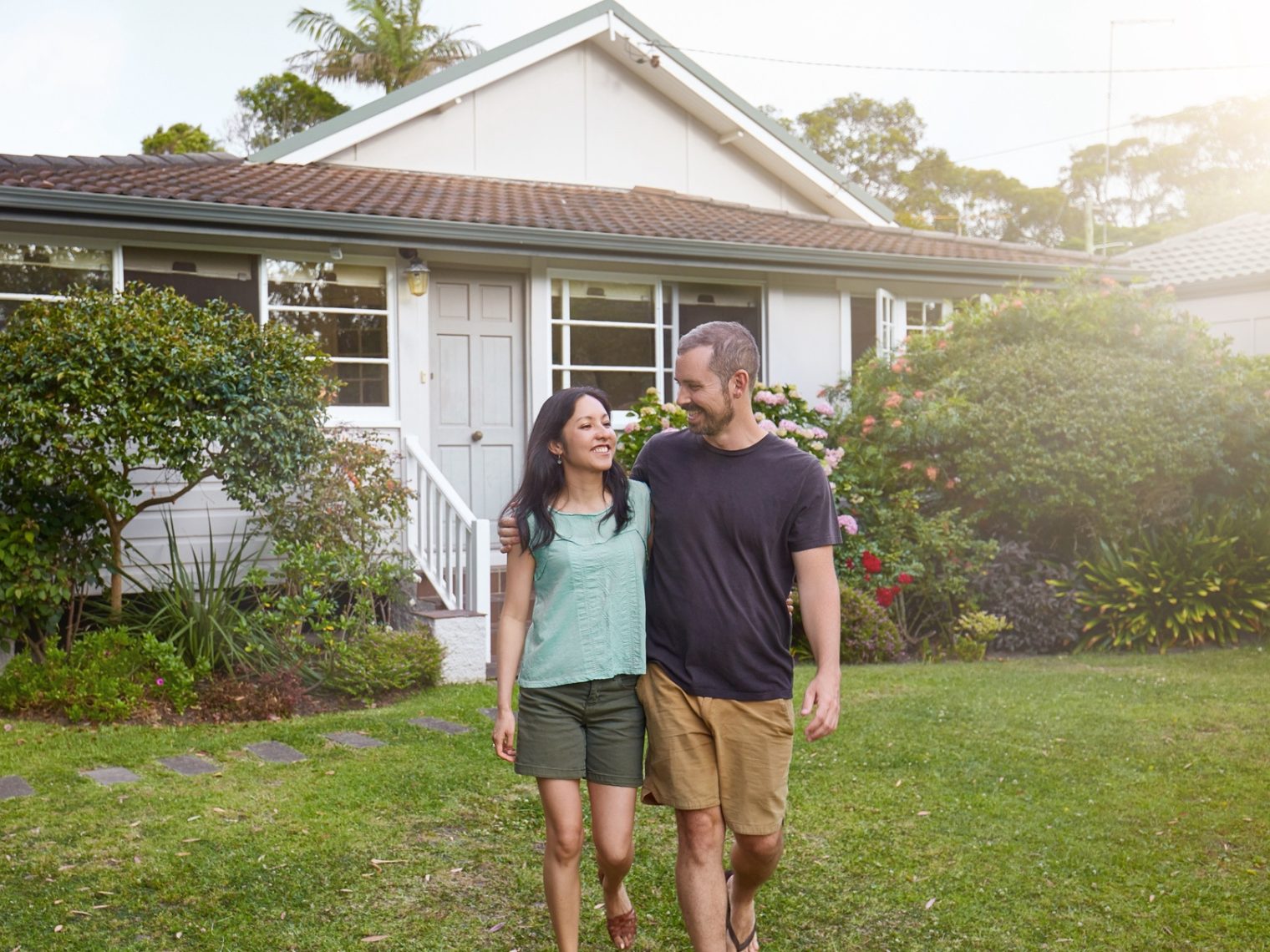 Happy mixed-race couple walking outside their front yard garden.