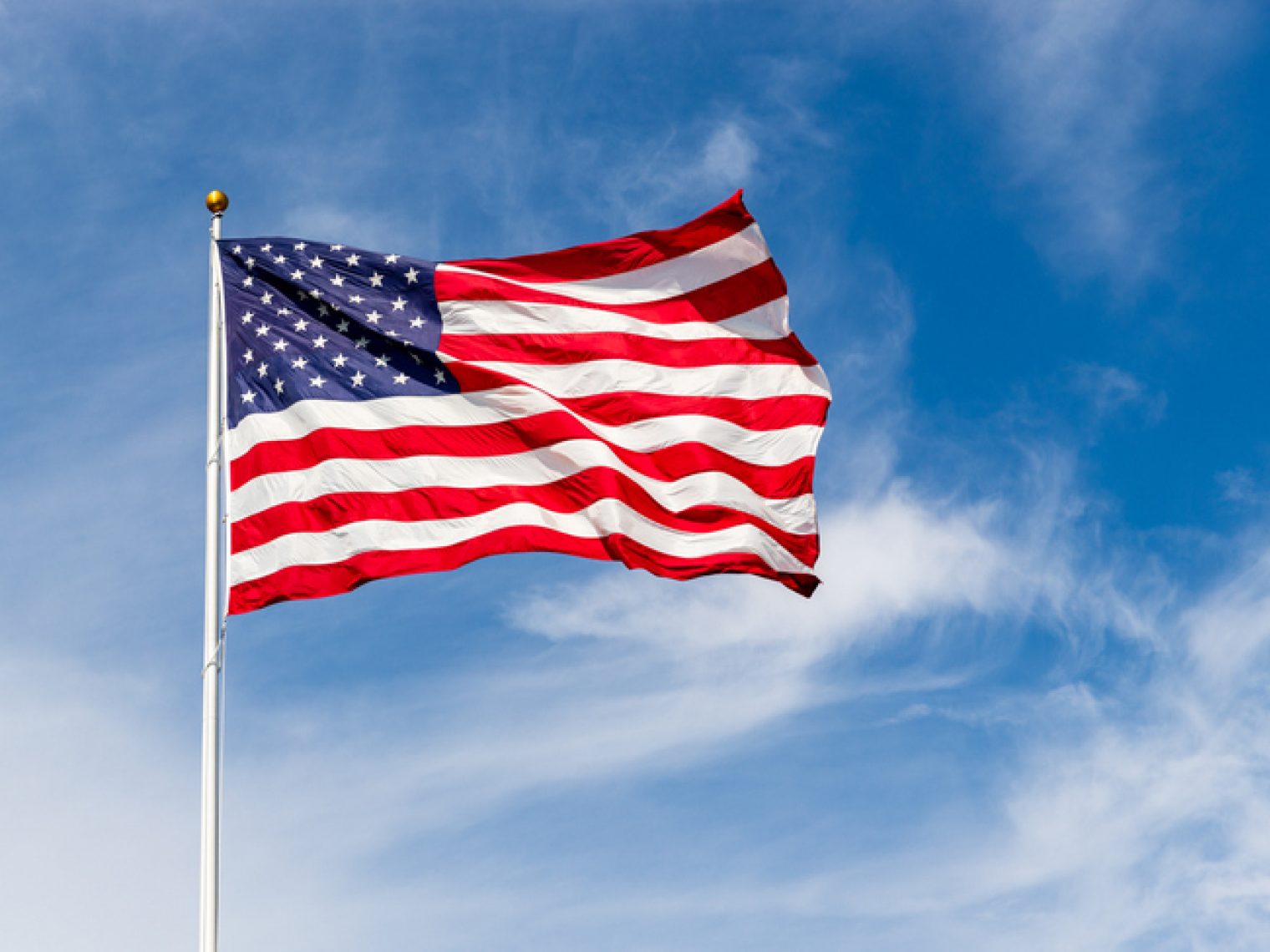 The United States flag is prominently displayed against a clear blue sky, waving in the wind on a bright day.