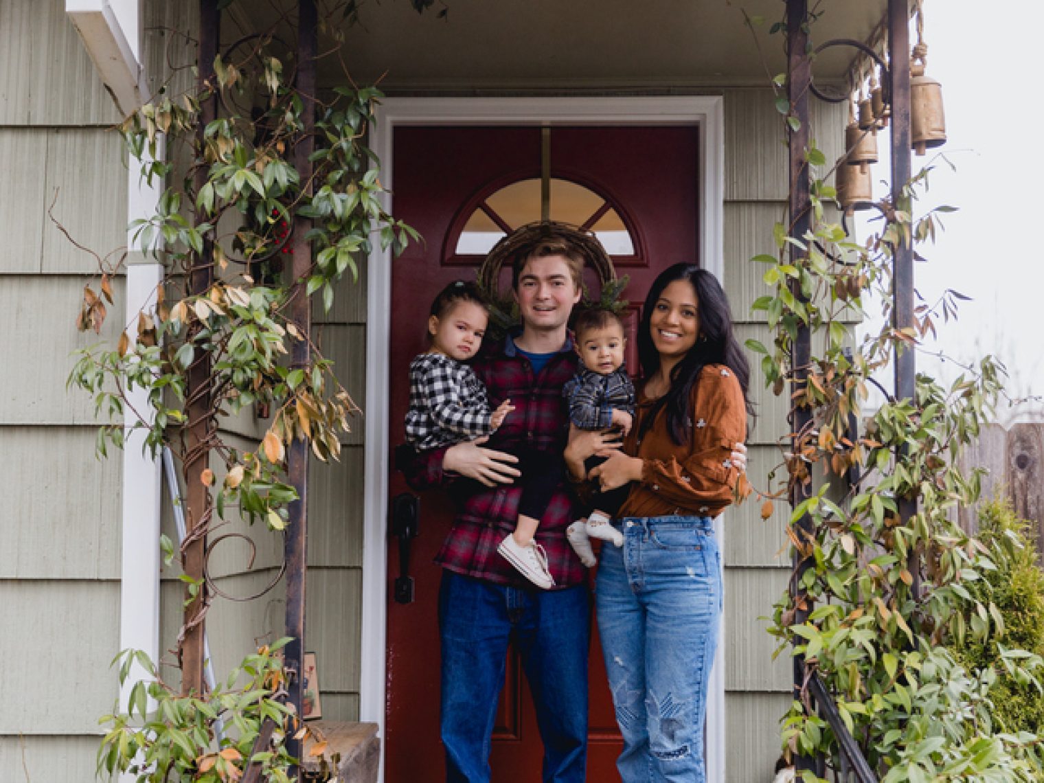 A cute multiracial young family with two kids in front of new home.