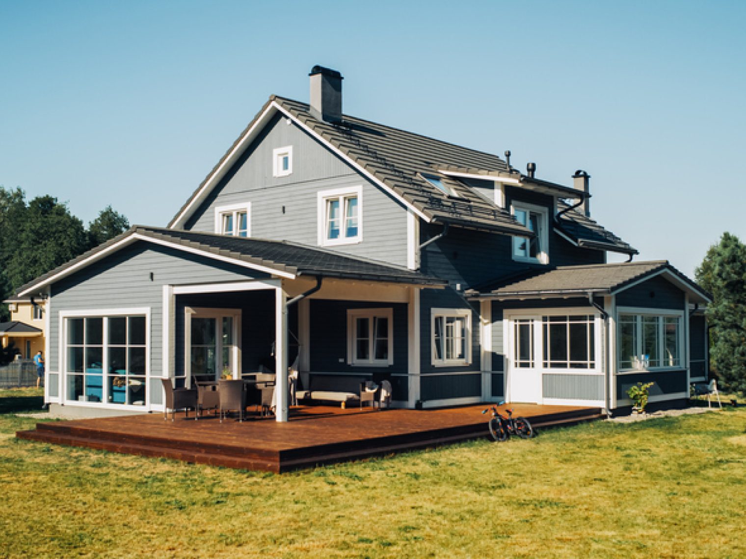 A charming two-story house with a spacious wooden deck and lawn, showcased on a sunny day.