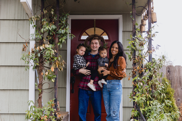 A cute multiracial young family with two kids in front of new home.